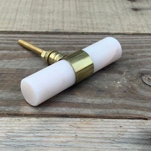 以下が含まれることがあります： 金色の金属製のバンドが付いた白い大理石のキャビネットノブ。ノブは丸く、背面にネジが付いています。