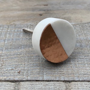 以下が含まれることがあります： 白と銅の丸いキャビネットノブで、ハンマード銅のアクセントが施されています。