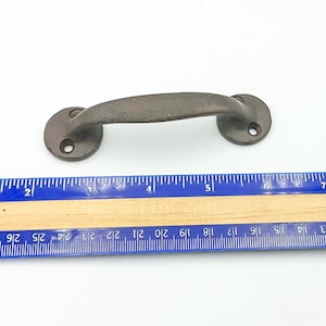 May include: A rustic, brown metal cabinet pull with a curved handle and two circular mounting plates. The pull measures approximately 6 inches in length. The hardware is designed for easy installation and adds a vintage touch to furniture.
