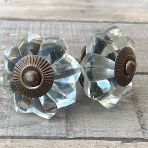 Peut inclure: Deux boutons de cabinet en verre transparent avec une finition en laiton. Les boutons ont un motif en étoile et un centre surélevé.