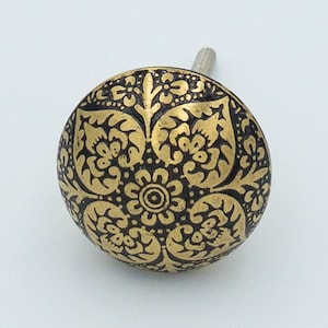 May include: A round, black and gold cabinet knob with a floral design.