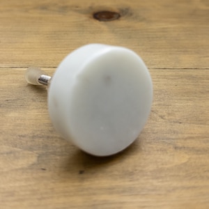 May include: White ceramic knob with a silver screw. The knob is round and has a smooth surface.