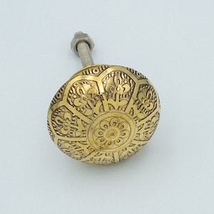 May include: A gold-toned cabinet knob with an intricate floral design. The knob is round and has a screw-on attachment.