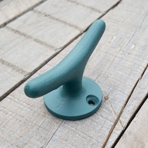May include: Teal blue metal hook shaped like a boat cleat. The hook is mounted on a round base and has a hole in the center.