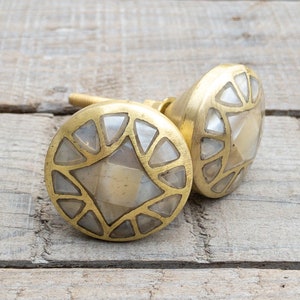 May include: Two gold-toned cabinet knobs with a geometric design. The knobs are made of brass and feature a mother-of-pearl inlay.