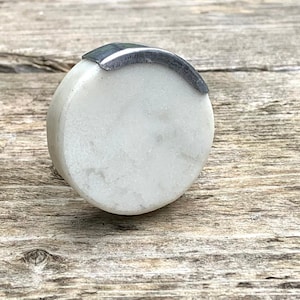 Peut inclure: Un bouton de porte rond en marbre blanc avec une bande en métal argenté autour du bord supérieur.