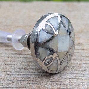 May include: A silver cabinet knob with a decorative inlay of white mother of pearl. The knob has a geometric design with a central square.