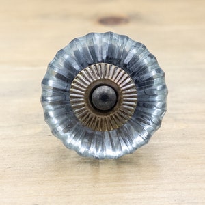 May include: A blue glass cabinet knob with a fluted design and a brass center. The knob has a dark gray metal screw.