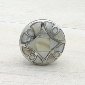 Peut inclure: Un bouton de porte rond en argent avec un motif décoratif en nacre blanche.