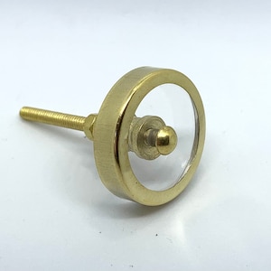 May include: Gold cabinet knob with a clear glass centre. The knob has a round shape and a screw on the back.