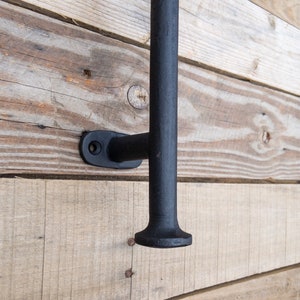 May include: Black metal door handle with a square base and a rounded top. The handle is mounted on a wooden wall.