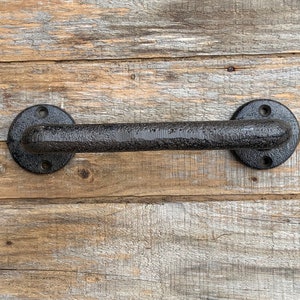 May include: A black, textured metal door handle featuring a horizontal bar design with two circular mounting plates at each end, each containing two pre-drilled screw holes for installation, showcasing a rugged, dark finish throughout the piece.