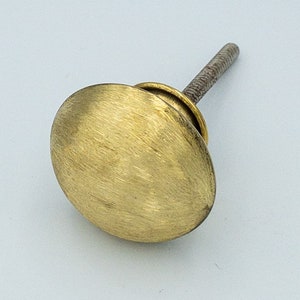 May include: A gold-colored, oval-shaped cabinet knob with a brushed finish. The knob is attached to a threaded metal rod. This hardware is suitable for drawers, cabinets, and other furniture.