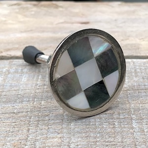 May include: A silver knob with a black and white checkered pattern made of mother of pearl. The knob is round and has a silver stem.