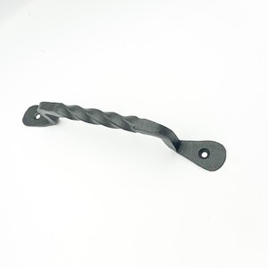 Peut inclure: Une poignée en métal torsadé gris foncé avec une surface texturée. La poignée a un design incurvé avec deux extrémités plates, chacune avec un seul trou pour le montage. La poignée est conçue pour une armoire ou un tiroir.