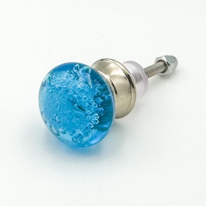 May include: A round cabinet knob featuring a bright blue glass sphere with internal air bubbles. The glass is attached to a metallic silver-toned base with a threaded metal bolt and a small nut extending from the back for installation purposes.