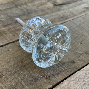 Peut inclure: Un bouton de porte de placard en verre transparent avec un motif floral décoratif. Le bouton est doté d'une vis en métal pour la fixation à une porte de placard.