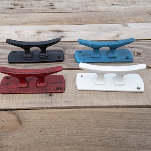 May include: Four cast iron boat cleat hooks in black, red, blue, and white. The hooks are mounted on a wooden surface.