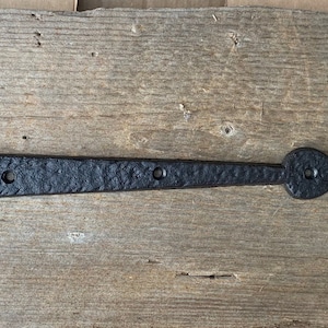 May include: Black metal hinge with a heart-shaped end. The hinge has four holes for attaching to a door or gate.