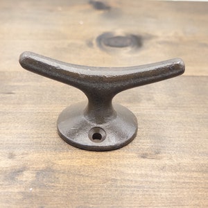 K&ouml;nnte beinhalten: Ein dunkelbrauner Bootshaken aus Gusseisen mit abgerundeter Basis. Der Haken ist so gestaltet, dass er einer Bootsklampe &auml;hnelt.