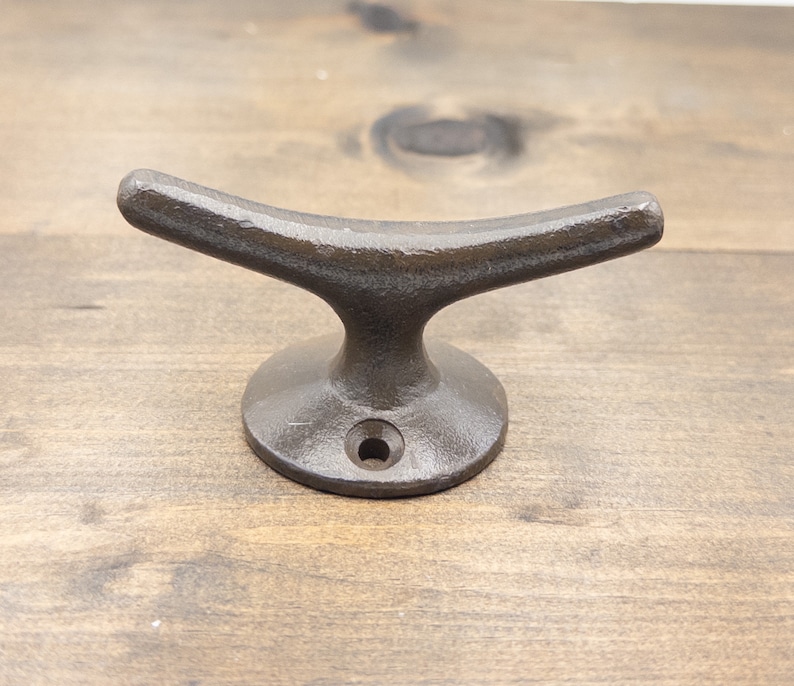 K&ouml;nnte beinhalten: Ein dunkelbrauner Bootshaken aus Gusseisen mit abgerundeter Basis. Der Haken ist so gestaltet, dass er einer Bootsklampe &auml;hnelt.