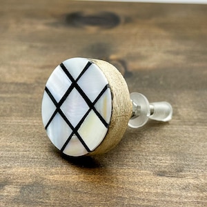 May include: A round, white and black cabinet knob with a wood base. The knob has a geometric pattern of black lines and white squares.