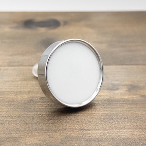May include: A silver-colored round tray with a white center. The tray is on a wooden surface.