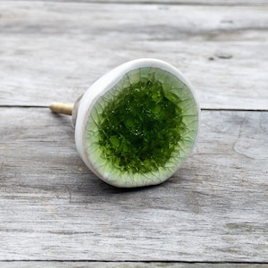 Peut inclure: Un bouton en céramique blanche avec un centre en verre vert. Le verre est brisé en petits morceaux, créant un effet de mosaïque.