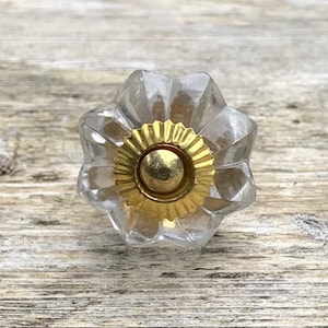Peut inclure: Un bouton de cabinet en verre transparent avec un centre en métal doré. Le bouton a une forme de fleur avec une surface texturée.