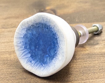 May include: White ceramic cabinet knob with a blue, crackled glaze in the center. The knob has a silver screw and a clear plastic washer.