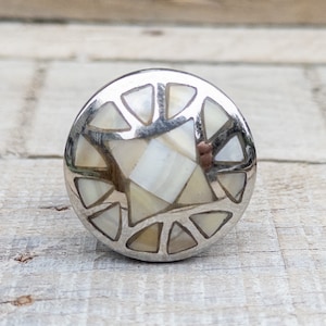 May include: A silver cabinet knob with a geometric design featuring a white and cream mother of pearl inlay.