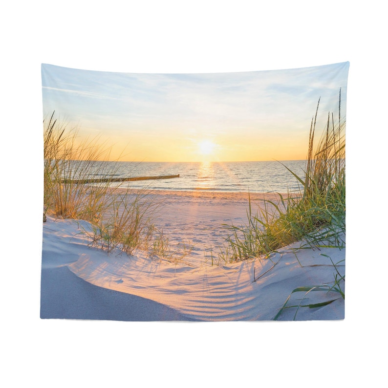 A serene beach scene at sunset, with the sun setting over the ocean and casting a warm glow on the sand and grassy dunes.