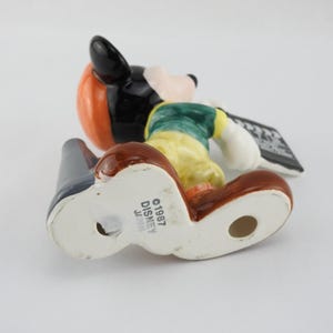 Peut inclure: Figurine Disney vintage de Mickey Mouse, portant un chapeau noir, des cheveux orange, une chemise verte et un pantalon jaune. La figurine tient une ardoise noire et est marqu&eacute;e "&copy;1987 DISNEY JAPAN". La figurine est en c&eacute;ramique et a une finition brillante.