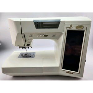 May include: A white Baby Lock Ellageo sewing machine featuring a large vertical touchscreen display on the right side, a needle assembly with a presser foot, a metal needle plate, and several control buttons located above the sewing area.