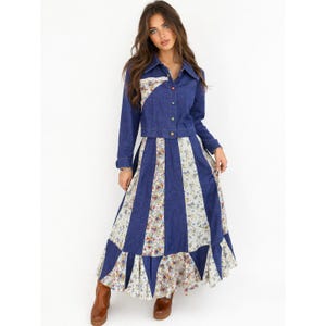 May include: A denim jacket and maxi skirt set. The jacket is a medium blue with a white floral pattern on the right shoulder. The skirt has vertical blue and white floral panels. The set has a vintage, bohemian style.