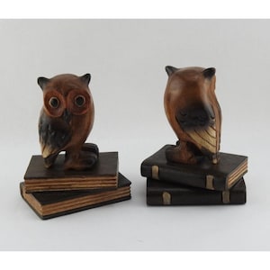May include: Two wooden owl bookends. Each owl is perched atop a stack of two books. The owls are brown with darker brown and black accents. The books are dark brown with tan-colored pages.