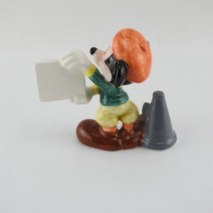 Peut inclure: Figurine en c&eacute;ramique d'une souris de dessin anim&eacute; tenant une pancarte blanche vierge. La souris porte une veste verte, un pantalon jaune et un chapeau orange. Un m&eacute;gaphone gris est pos&eacute; &agrave; c&ocirc;t&eacute; de la souris sur une base marron. La figurine est de collection.