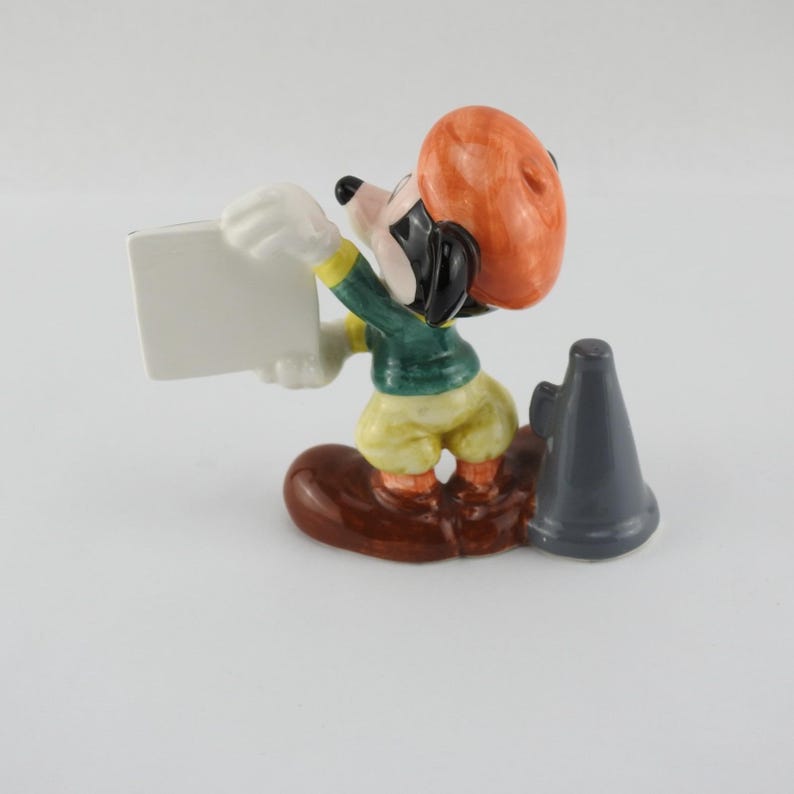 Peut inclure: Figurine en c&eacute;ramique d'une souris de dessin anim&eacute; tenant une pancarte blanche vierge. La souris porte une veste verte, un pantalon jaune et un chapeau orange. Un m&eacute;gaphone gris est pos&eacute; &agrave; c&ocirc;t&eacute; de la souris sur une base marron. La figurine est de collection.