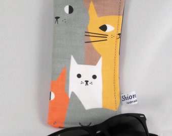 May include: A gray, orange, yellow, and white fabric eyeglasses case with a pattern of cats. The case has a black zipper and a small tag that says "Shion handmade". A pair of black sunglasses are lying next to the case.