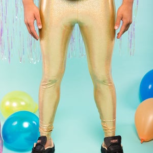 May include: Gold metallic leggings with a subtle iridescent sheen. The leggings are worn by a person standing on a light blue background with balloons.