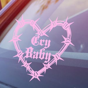May include: Pink vinyl sticker with a barbed wire heart design and the text "Cry Baby" inside the heart.