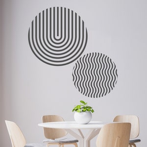 May include: A white round table with four light wood chairs and a small potted plant. The wall behind the table has two black and white geometric designs.
