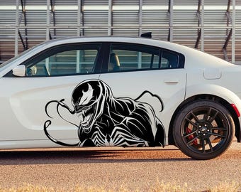 May include: A white car with a black and white graphic of a superhero character on the side. The character is a black silhouette with white eyes and teeth.