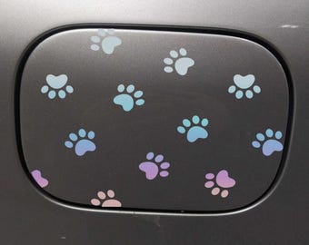 May include: A gray car gas tank door with a pattern of pastel blue, pink, and purple paw prints.