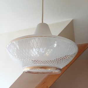 May include: White glass pendant light fixture with a gold trim and a geometric pattern. The light fixture is hanging from a white ceiling.