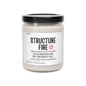 Peut inclure: Un bocal de bougie blanc avec un couvercle noir et une étiquette blanche sur laquelle est inscrit "STRUCTURE FIRE" avec un logo de pompier rouge. L'étiquette indique également "POUR LE POMPIER QUI NE FAIT QUE DES APPELS MÉDICAUX... AU CAS OÙ VOUS AURIEN OUBLIÉ L'ODEUR DU VRAI FEU".