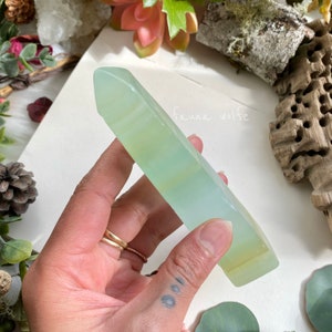 Puede incluir: Una punta de cristal verde claro, transl&uacute;cida, pulida, con una punta puntiaguda y una base plana. La punta de cristal se sostiene en una mano.