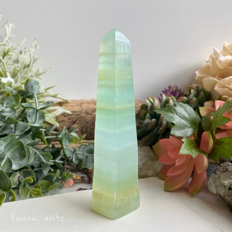 Puede incluir: Una punta de cristal obelisco con bandas verde claro y blanco. El cristal es liso y pulido.