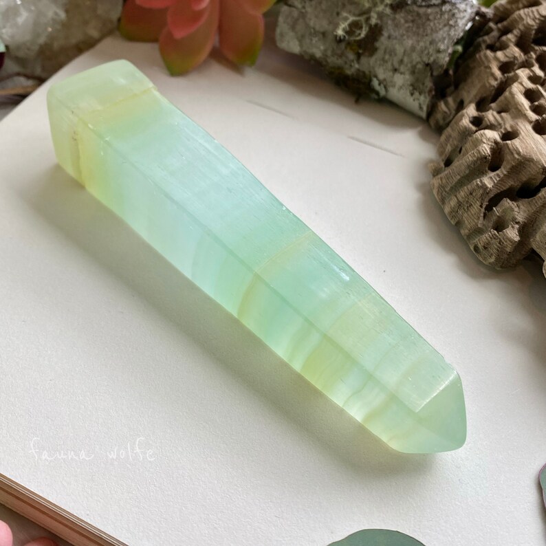 Puede incluir: Una punta de cristal verde claro y blanco con una punta puntiaguda. El cristal es liso y pulido.