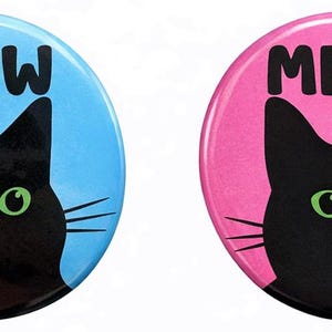 May include: Two circular badges featuring a black cat design. One has a light blue background, the other is pink. Both badges display the word "MEOW" in black above the cat's head.